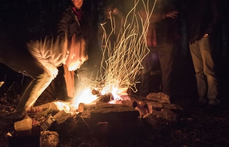 Sparks fly from a campfire as Matt McWilliams leans over to stoke the fire.