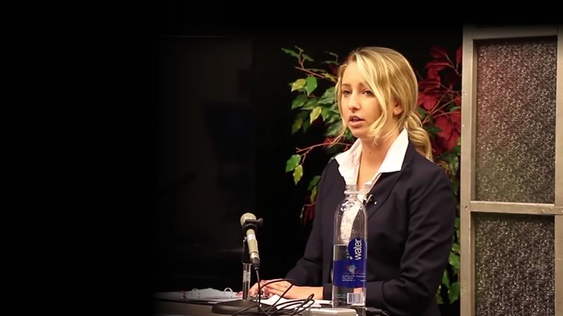 A student stands at a podium and answers questions during a news conference Hot Seat exercise.