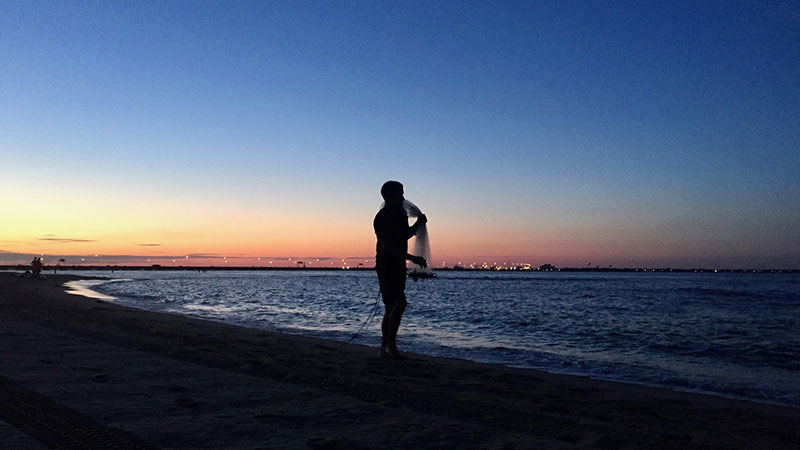 A man silhouetted by the setting sun stands on the Chesapeake Bay with a fishing net